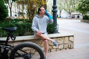 vol lengte mannetje fietser drinken water in de stad. elektrisch motor, elektrische fiets, elektrisch fiets fiets Aan de voorgrond foto