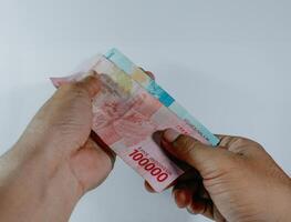 Indonesisch munteenheid. hand- Holding 100.000 en 50.000 roepia bankbiljetten Aan een wit achtergrond. foto