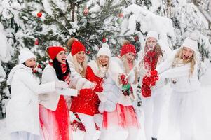 een groot groep van meisjes met bril van Champagne in hun handen staat in de winter bos.meisjes in rood en wit kleren met nieuw jaar drankjes in een met sneeuw bedekt Woud. foto