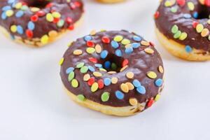 reeks van bruin chocola donut versierd met smarties geïsoleerd Aan wit achtergrond kant visie. gebakken deeg confectie, toetje voedsel, zoet tussendoortje met chocola beglazing en snoepjes. selectief focus foto