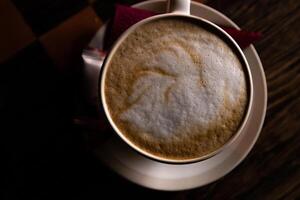 detailopname van de kop van cappuccino Aan de wit bord Aan de donker houten tafel. wit kop van heet koffie latte top visie. kopiëren ruimte. foto