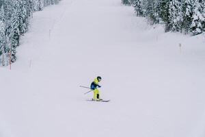 kind in een geel ski pak skis naar beneden een berg helling, leunend naar de kant foto