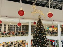 Podgorica, Montenegro - 25 december 2022. hert beeldje en sprookjesachtige lichten zijn gehecht naar de plafond bovenstaand een Kerstmis boom in een winkelcentrum foto