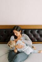 mam borstvoeding een weinig meisje knuffelen haar in haar armen terwijl zittend Aan de bed foto