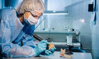 een gemaskeerd en gehandschoende tandheelkundig technicus werken Aan een prothetisch tand in zijn laboratorium foto