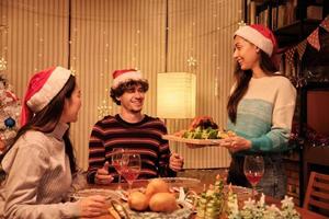 een speciale familiemaaltijd, jonge vrouw serveert geroosterde kalkoen aan vrienden en vrolijk met drankjes tijdens een diner in de eetzaal van het huis die is ingericht voor kerstfestival en nieuwjaarsfeest. foto