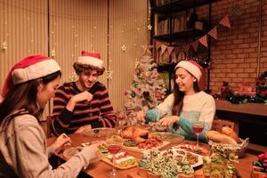 vrienden genieten van een leuk diner aan tafel met speciale gerechten, jonge vrouw die geroosterde kalkoen snijdt in de eetkamer van huis, versierd met ornamenten, kerstfestival en nieuwjaarsfeest. foto