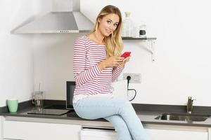 lachende mooie vrouw die haar smartphone thuis in de keuken gebruikt