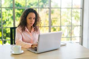 Latijnse vrouw die met laptop en papier op werkruimte werkt