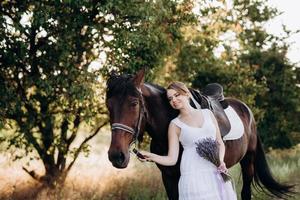 meisje in een witte zomerjurk op een wandeling met bruine paarden foto