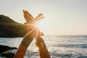 vrouw zee yoga. gelukkig vrouw in wit zwempak en boho stijl armbanden beoefenen buitenshuis Aan yoga mat door zee Aan zonsondergang. Dames yoga geschiktheid routine. gezond levensstijl, harmonie en meditatie foto