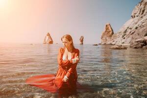 vrouw reizen zee. gelukkig toerist in rood jurk genieten nemen afbeelding buitenshuis voor herinneringen. vrouw reiziger poseren in zee strand, omringd door vulkanisch bergen, sharing reizen avontuur reis foto