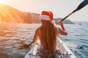 vrouw in kajak terug visie. gelukkig jong vrouw in de kerstman hoed drijvend in kajak Aan kalmte zee. zomer vakantie vakantie en vrolijk vrouw mensen ontspannende hebben pret Aan de boot. foto