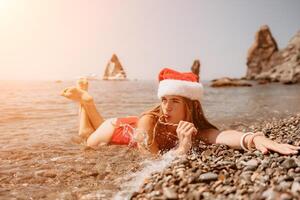 vrouw reizen zee. gelukkig toerist genieten nemen afbeelding Aan de strand voor herinneringen. vrouw reiziger in de kerstman hoed looks Bij camera Aan de zee baai, sharing reizen avontuur reis foto