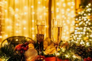 twee Champagne bril gevulde met Champagne zijn geplaatst Aan een tafel in de buurt naar Kerstmis boom. de bril zijn omringd door lichten, creëren een feestelijk atmosfeer. foto