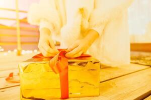 een vrouw in een wit jurk is Holding een goud doos met een rood lintje. ze is vervelend een kroon Aan haar hoofd. de vrouw verschijnt naar worden opening de geschenk doos. foto