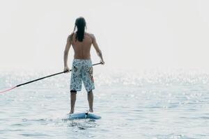 Mens sup zee. sterk atletisch Mens leert naar peddelen sup staand Aan bord in Open zee oceaan Aan zonnig dag. zomer vakantie vakantie en reizen concept. antenne visie. langzaam beweging foto