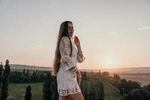 gelukkig vrouw in wit boho jurk Aan zonsondergang in bergen. romantisch vrouw met lang haar- staand met haar terug Aan de zonsondergang in natuur in zomer met Open handen. silhouet. natuur. zonsondergang. foto