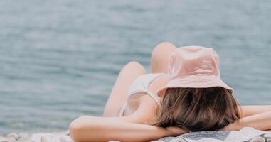 onherkenbaar positief vrouw in wit bikini zonnen of bruinen Aan kust strand gedurende zomer. gelukkig toerist genieten van zon bruinen aan het liegen Aan strand stoel lounge Bij luxe toevlucht foto