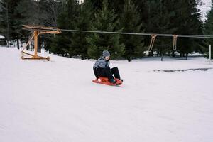 lachend jong vrouw haast Aan een slee naar beneden een besneeuwd helling Verleden een touw optillen foto