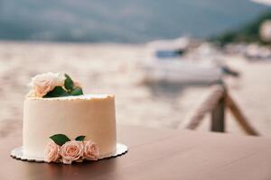 bruiloft taart versierd met rozen staat Aan een staan Aan een tafel Aan een pier door de zee foto
