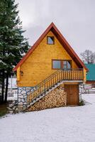 twee verdiepingen houten huisje met een houtstapel onder de stappen in een besneeuwd Woud foto