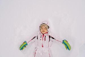 weinig meisje maakt een sneeuw engel aan het liegen in een sneeuwjacht met haar ogen Gesloten foto