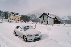 met sneeuw bedekt auto met verheven voorruit ruitenwissers staat in de buurt kleurrijk huizen Bij de voet van de bergen foto