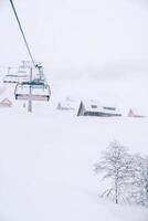 vierzitter stoeltjeslift stijgt een met sneeuw bedekt berg met houten hutten foto