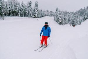skiër in een ski pak en helm skis naar beneden de helling van een besneeuwd berg foto
