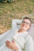 jong glimlachen Mens leugens in een hangmat in de tuin met zijn hand- onder zijn hoofd foto