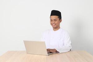 portret van opgewonden Aziatisch moslim Mens in koko overhemd met kalotje werken Aan zijn laptop gedurende vastend Aan Ramadan maand. geïsoleerd beeld Aan wit achtergrond foto