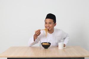 portret van aantrekkelijk Aziatisch moslim Mens aan het eten smaakvol ogenblik noedels met eetstokjes geserveerd Aan schaal. iftar en pre dageraad maaltijd concept. geïsoleerd beeld Aan wit achtergrond foto