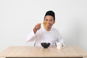 portret van aantrekkelijk Aziatisch moslim Mens aan het eten smaakvol ogenblik noedels met eetstokjes geserveerd Aan schaal. iftar en pre dageraad maaltijd concept. geïsoleerd beeld Aan wit achtergrond foto