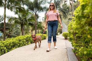 een vrolijk vrouw wandelingen haar hond in een tropisch stedelijk park. foto