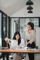 twee vrouw echt landgoed professionals bespreken project details met een model- huis Aan de tafel, symboliseert project planning en teamwerk. foto