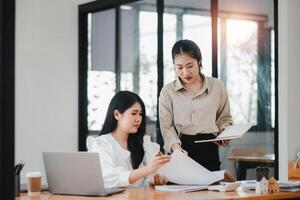 twee professioneel Dames innemend in een samenwerkend werk discussie met laptops en aantekeningen Aan een helder kantoor bureau. foto