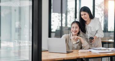 twee glimlachen vrouw collega's gezamenlijk werken Aan een project met een laptop en koffie in een helder kantoor ruimte. foto