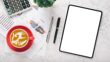 een goed georganiseerd bureau met een tablet met een blanco scherm, artistiek latte in een rood beker, rekenmachine, pen, en financieel samenvattingen Aan papier, allemaal boven een gepolijst marmeren achtergrond. foto