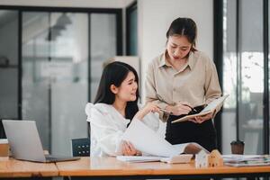 twee professioneel Dames innemend in een samenwerkend werk discussie met laptops en aantekeningen Aan een helder kantoor bureau. foto