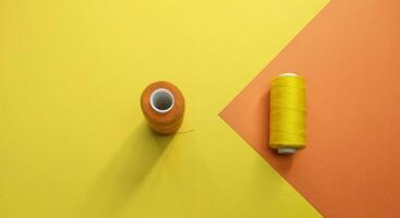spoelen van draad en een naald- Aan een geel en oranje achtergrond, contrast consept foto