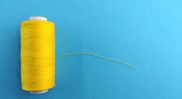 spoelen van draad en een naald- Aan een geel en blauw achtergrond, contrast consept foto