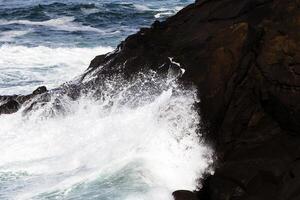 strak schot van golven het wassen omhoog Aan lava rots foto