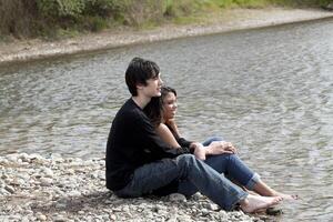 tiener paar zittend Aan steenachtig rivier- bank foto