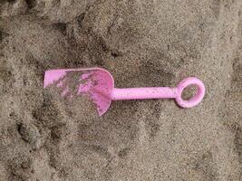 klein plastic roze Schep aan het liegen in zand foto