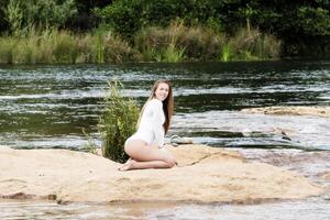 Kaukasisch tiener vrouw zittend Aan aarde in rivier- wit turnpakje foto
