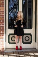 aantrekkelijk jong blond vrouw staand zwart jurk rood schoenen foto