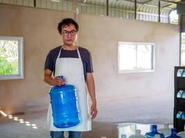 Aziatisch Mens arbeider of kwaliteit inspecteur in werkkleding werken in controle drinken water blauw gallon in drinken water fabriek voordat zending.drinken water zakelijk, klein bedrijf, winkel, magazijn foto