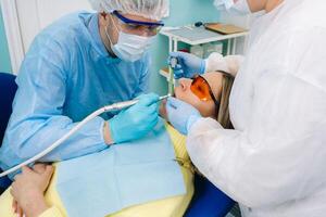 een mannetje tandarts met tandheelkundig gereedschap boren de tanden van een geduldig met een assistent. de concept van geneesmiddel, tandheelkunde en gezondheidszorg foto