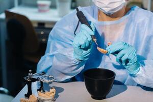 een tandheelkundig technicus in beschermend kleding is werken Aan een prothetisch tand in zijn laboratorium foto